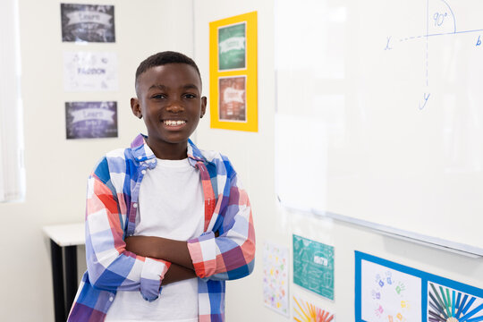 Confident african american boy smiling in classroom, standing by whiteboard with equation, at school