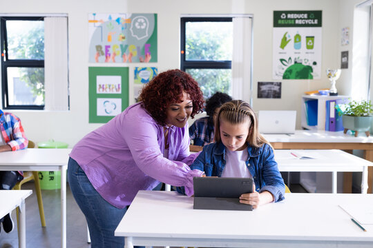 Female teacher helping girl with tablet in classroom, focusing on digital learning, at school