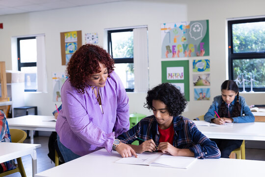 Female teacher helping boy with homework in classroom, other diverse students studying, at school - Powered by Adobe