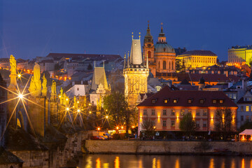 Evening view of Charles Bridge and Old Town in Prague, Czech Republic with illuminated buildings and river reflections