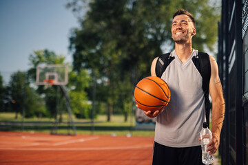 Naklejka premium Smiling basketball player holding ball on outdoor court after training