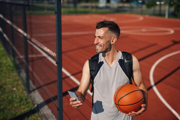 Naklejka premium Smiling basketball player using smartphone on outdoor court after training