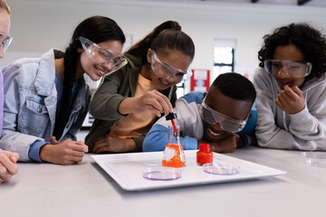 Diverse students in science class experimenting with beaker, wearing safety goggles, at school