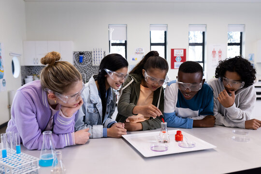 In school, diverse students wearing safety goggles conducting science experiment in classroom