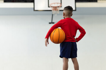 Young boy holding basketball in gym, preparing to shoot at hoop, copy space