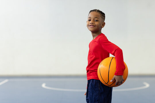 Smiling boy holding basketball on court, enjoying school sports activity, copy space