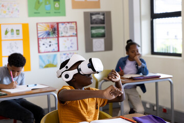 In classroom, african american boy using VR headset while classmates study at desks, at school