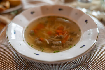 A white plate with soup containing meat dumplings, carrots, and noodles. 
