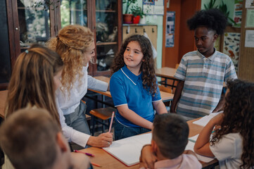Teacher helping young girl student during class in elementary school classroom