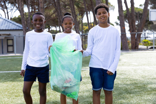 Cleaning up school playground, diverse students holding trash bag, smiling and helping environment