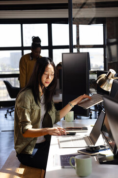Asian woman coding on laptop in modern office, focused on work