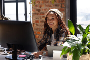 Smiling woman coding at desk with computer and plants in modern office