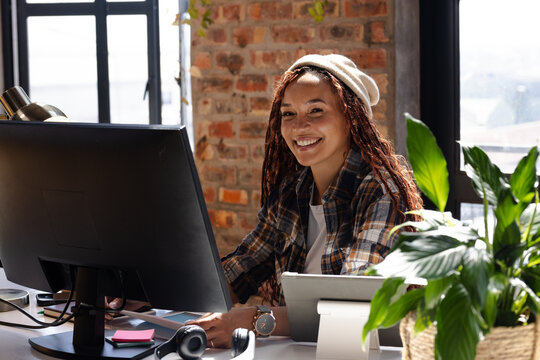 Smiling woman coding at desk with computer and plants in modern office