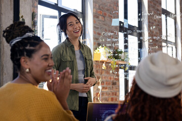 Asian woman leading coding workshop, smiling and engaging with diverse team, at office