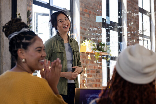Asian woman leading coding workshop, smiling and engaging with diverse team, at office