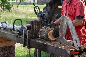 Farmer wearing gloves and red workwear operates a tractor driven hydraulic log splitter,...