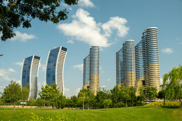 Modern Skyscrapers and Residential Towers Rising Above Green Park in Istanbul Turkey on Sunny Day with Blue Sky and White Clouds Framed by Lush Trees
