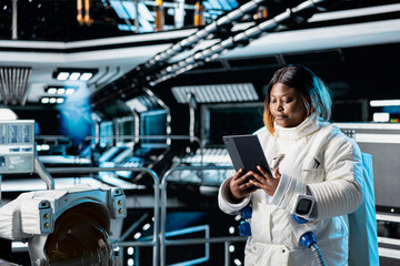 Female cosmonaut updating flight log on tablet, preparing for planetary mission outside. Astronaut studying star charts before beginning landing procedures on solar system planet