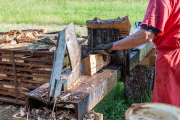 Lumberjack wearing gloves is splitting firewood logs with a hydraulic machine in a rural...