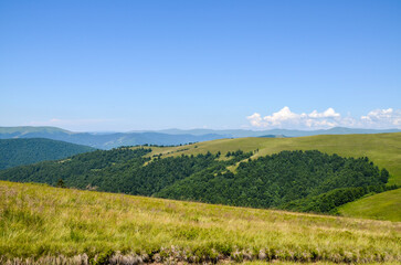 Rolling green hills and dense forests extend under a brilliant blue sky, creating a peaceful and...