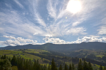 Tranquil view of rolling hills under blue sky adorned with wispy clouds and sunlight. Serene setting conveys natural beauty and peace, highlighting harmony in the countryside environment. Carpathians