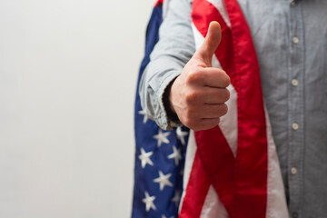 Close-up of a man making a thumbs up gesture with an American flag. Support and patriotic spirit.