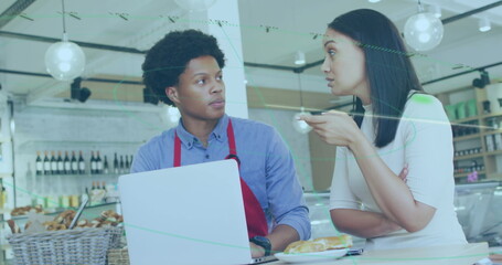 Male cafe staff interacting with female customer at bakery counter, with laptop and pastries