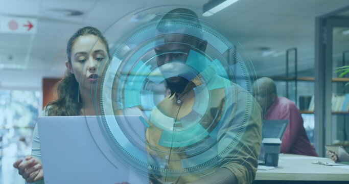 Examining team collaborating on silver laptop screen in modern office, featuring interface graphic
