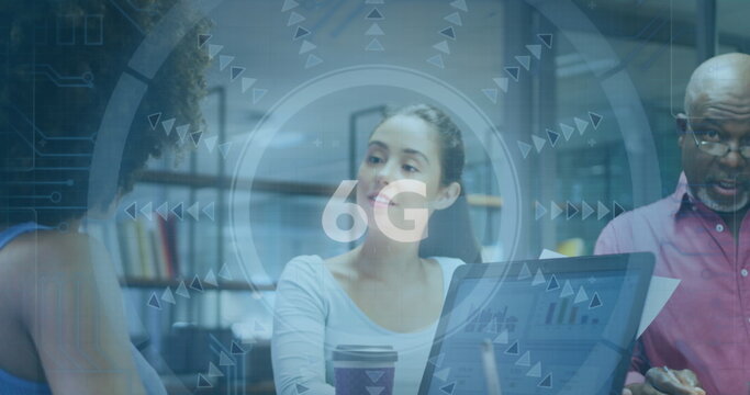 Colleagues discussing and analyzing charts on laptops at table in meeting room, with 6G overlay - Powered by Adobe