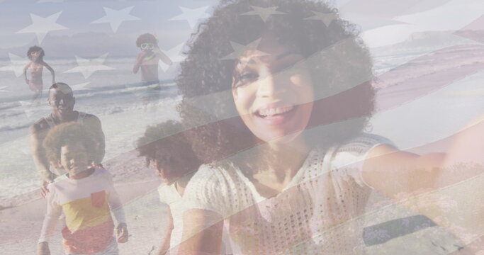 Taking woman in white top extending arm for selfie at sandy shoreline, with smartphone, flag motif