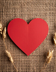 A handmade red paper heart contrasted against the texture of rough hessian fabric background.