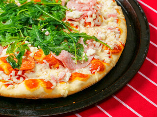 A pizza with ham and spinach on a black tray. The pizza is sitting on a red and white stripe table...
