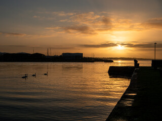 Spectacular sun rise scene over Galway bay, Ireland. Rich colorful cloudy sky. Calm ocean water with sky and sun reflection. Nobody. Relaxed and peaceful mood. Irish landscape. Swans glide to ocean