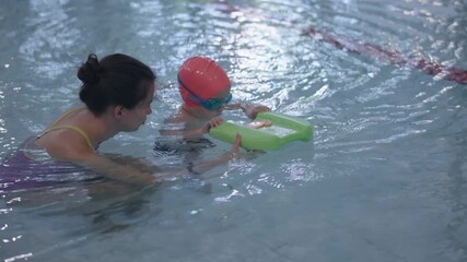 A young child is learning how to swim with the guidance of a very supportive instructor in a swimming pool setting
