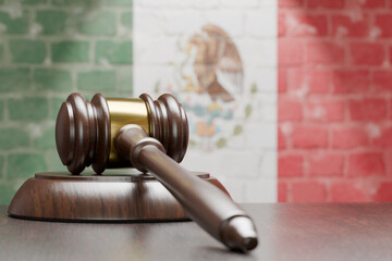 Wooden Gavel Resting on Table In Front of A Brick Wall with Mexican Flag.
