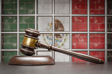 Wooden Gavel Resting on Table In Front of Prison Bars and A Brick Wall with Mexican Flag.