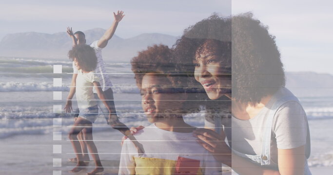 Gazing mother and daughter kneeling near shoreline, with father and son stepping through surf - Powered by Adobe