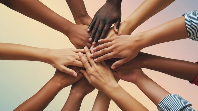 Diverse group of people showing different skin tones with their hands stacked for unity and teamwork gesture.