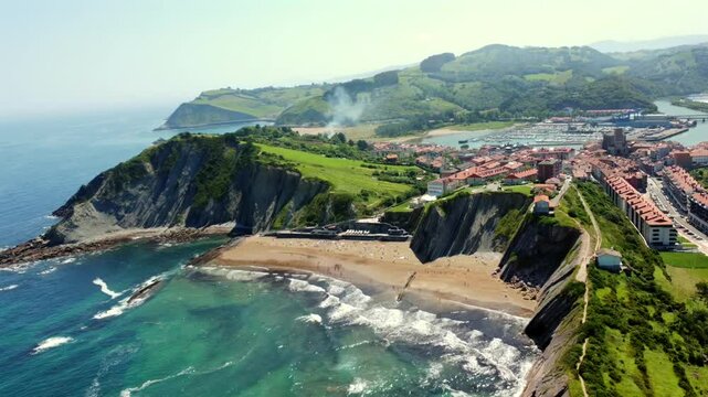 Scenic aerial flyover revealing zumaia's dramatic itzurun beach, rugged coastline, and expansive cantabrian sea under clear sunny skies