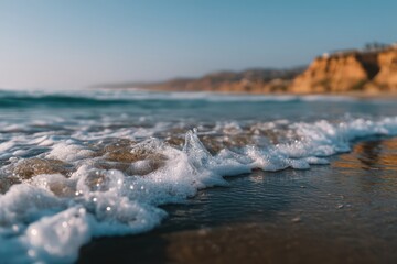 Obraz premium Gentle ocean waves crashing onto golden sandy beach at sunset creating a serene coastal landscape with warm sunlight reflecting off the water inviting relaxation and deep thoughts