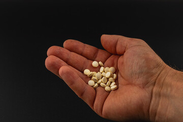 Hand holding white tablets against a dark background