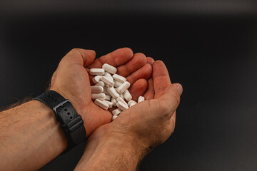 Hands holding white tablets against a dark background
