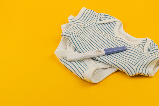 Baby clothes and pregnancy test on bright yellow background