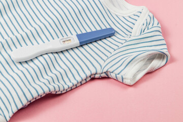 Pregnancy test on striped onesie with pink backdrop