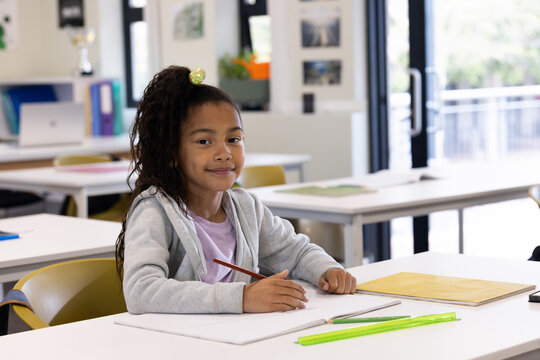 African American girl holding pencil, writing in open notebook at bright classroom desk with ruler