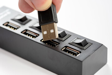 Closeup of a hand plugging in a USB cable into a black multi-port usb hub with power switches,...