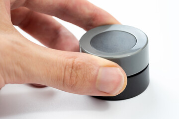 Finger adjusting a modern round grey black control knob isolated on white, closeup of a human hand turning a simple round dial, generic electronic device settings, volume control interface concept