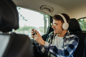 Young caucasian man student traveling on backseat in car with wireless headphones 