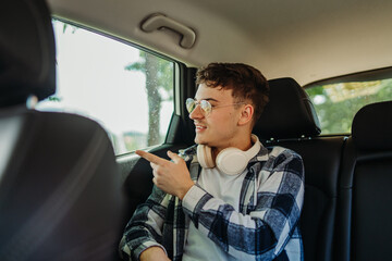 Young caucasian man student traveling on backseat in car with wireless headphones 