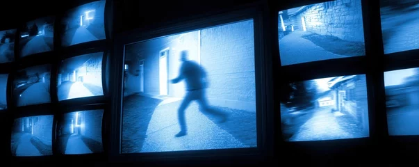 A series of surveillance monitors showing various night-time security camera footage, with one screen highlighting a blurred figure running. © JT Studio